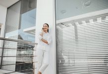 the girl is standing at the window with the blinds closed